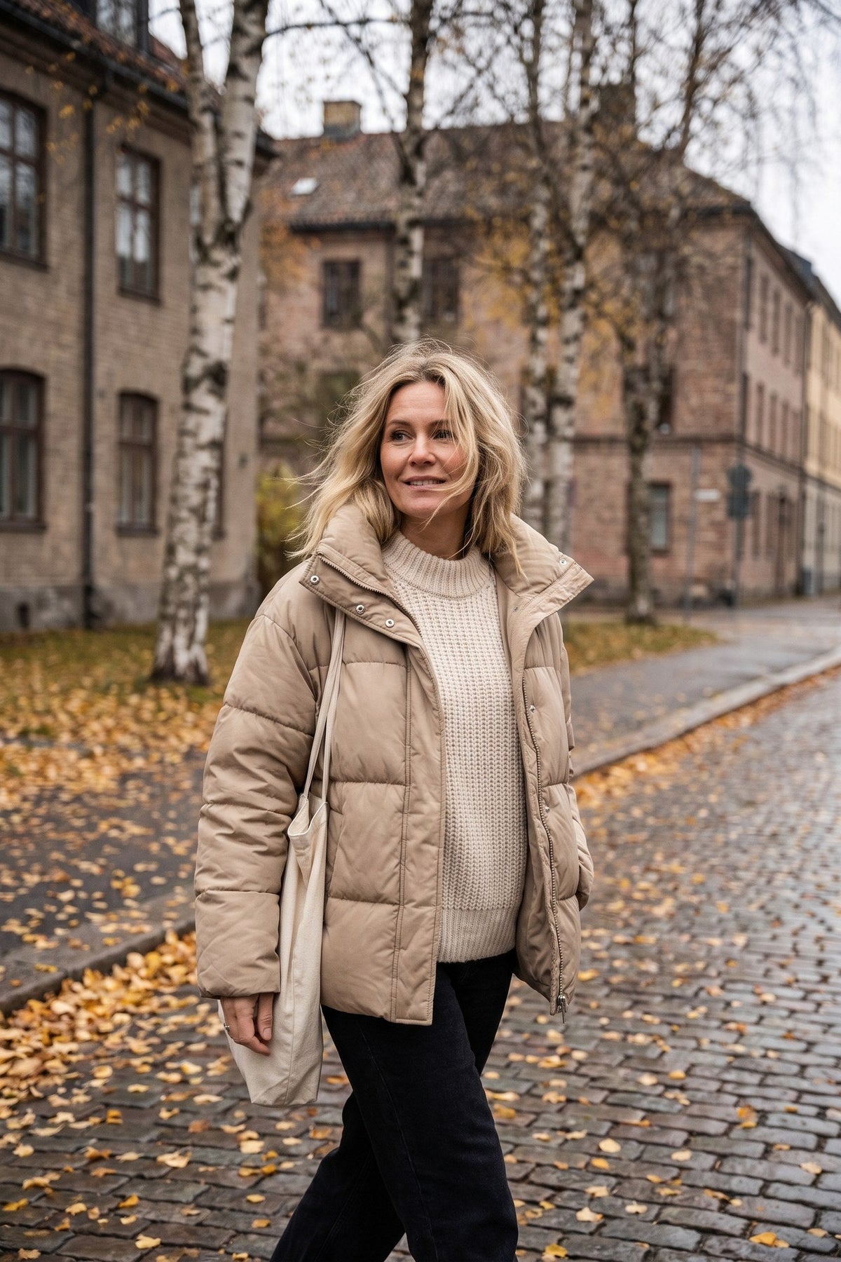 Kvinna i beige kviltad höstjacka på en lövtäckt gata i höstljus