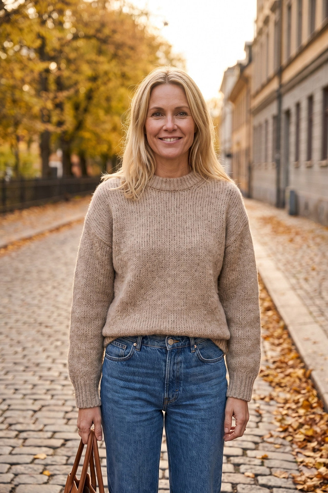 Kvinna i beige oversized stickad tröja och raka jeans i höstljus