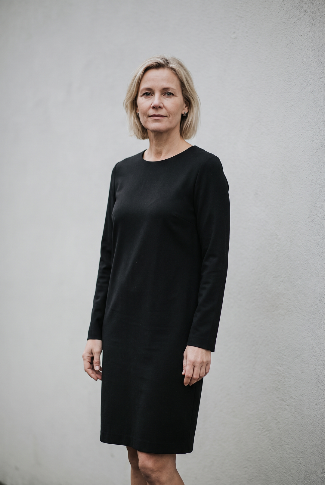 Kvinna i svart långärmad knälång klänning med enkelt smycke i ett stilla dagsljus