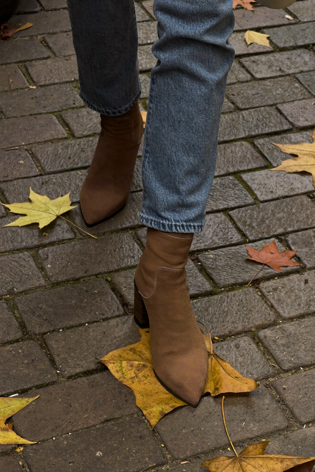 Kvinna i bruna mockaankelboots och raka jeans på en gata täckt av höstlöv