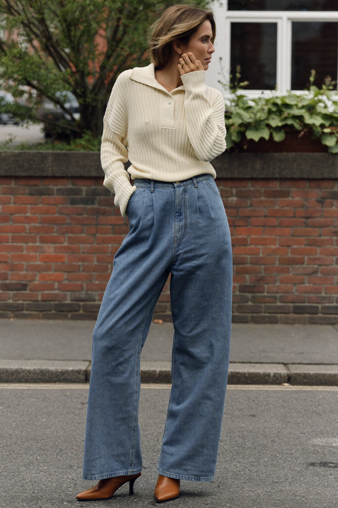 Kvinna i högmidjade jeans med vida ben, instoppad krämfärgad ribbstickad tröja och ljusbruna boots på en höstgata