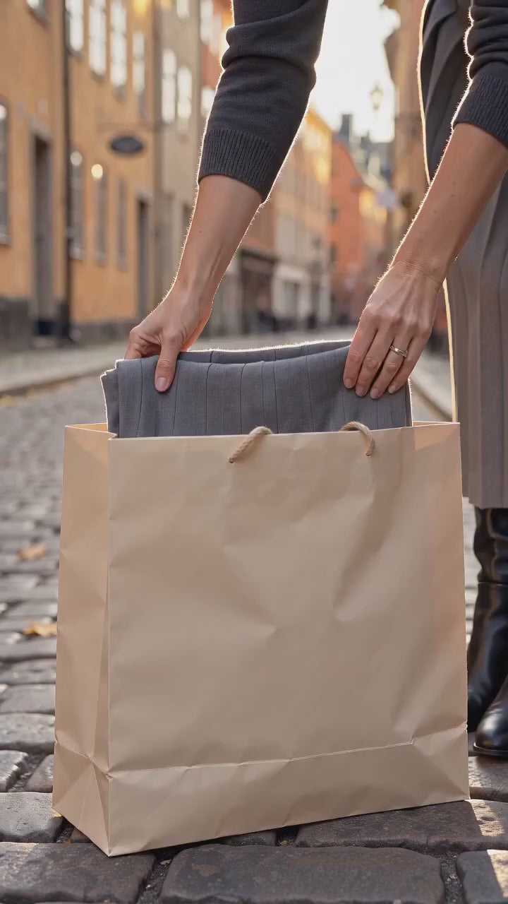 Kvinna i grå plisserad midikjol med smalt svart bälte, mörkgrå stickad tröja och svarta boots på en kullerstensgata