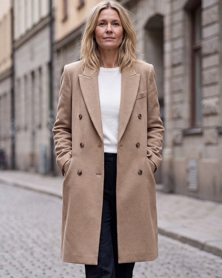 Kvinna i lång beige dubbelknäppt kavajjacka med strukturerade axlar på stadsgata