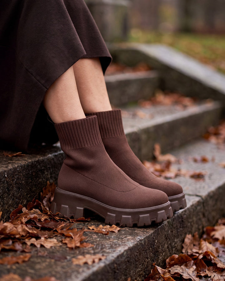 Bruna stickade sockboots med grov platåsula på stentrappa täckt av höstlöv